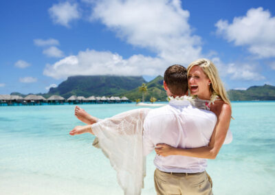 photo d'un mari portant sa femme en robe de mariée dans l'eau