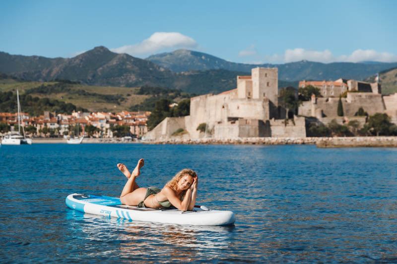 Session photo d'Aurélie en maillot de bain allongée sur un Stand-Up Paddle devant la ville de Collioure